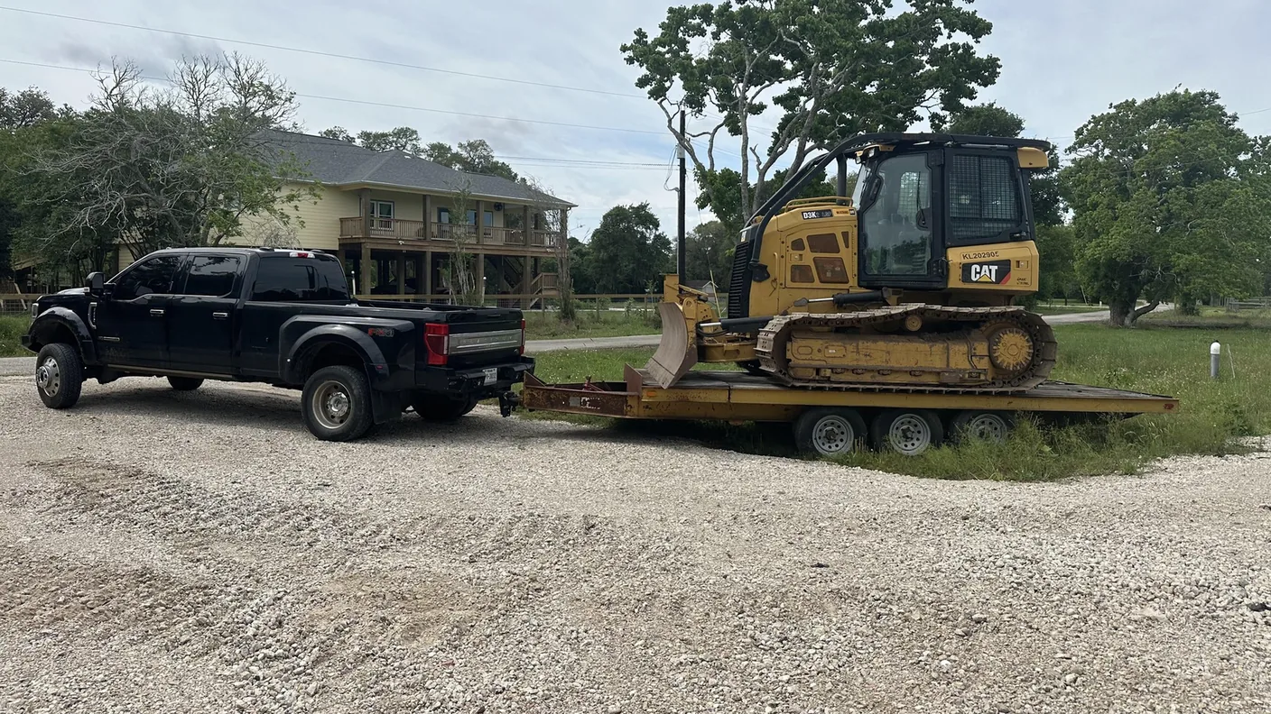 Pickup truck and trailer carrying a dozer on a gravel drive, land clearing