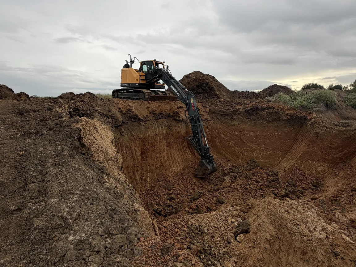 Excavator digging deep into red clay, dirt work