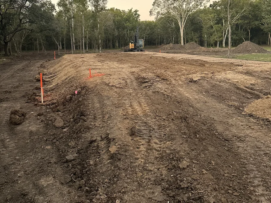 Raised building pad with grade stakes and an excavator behind, dirt work