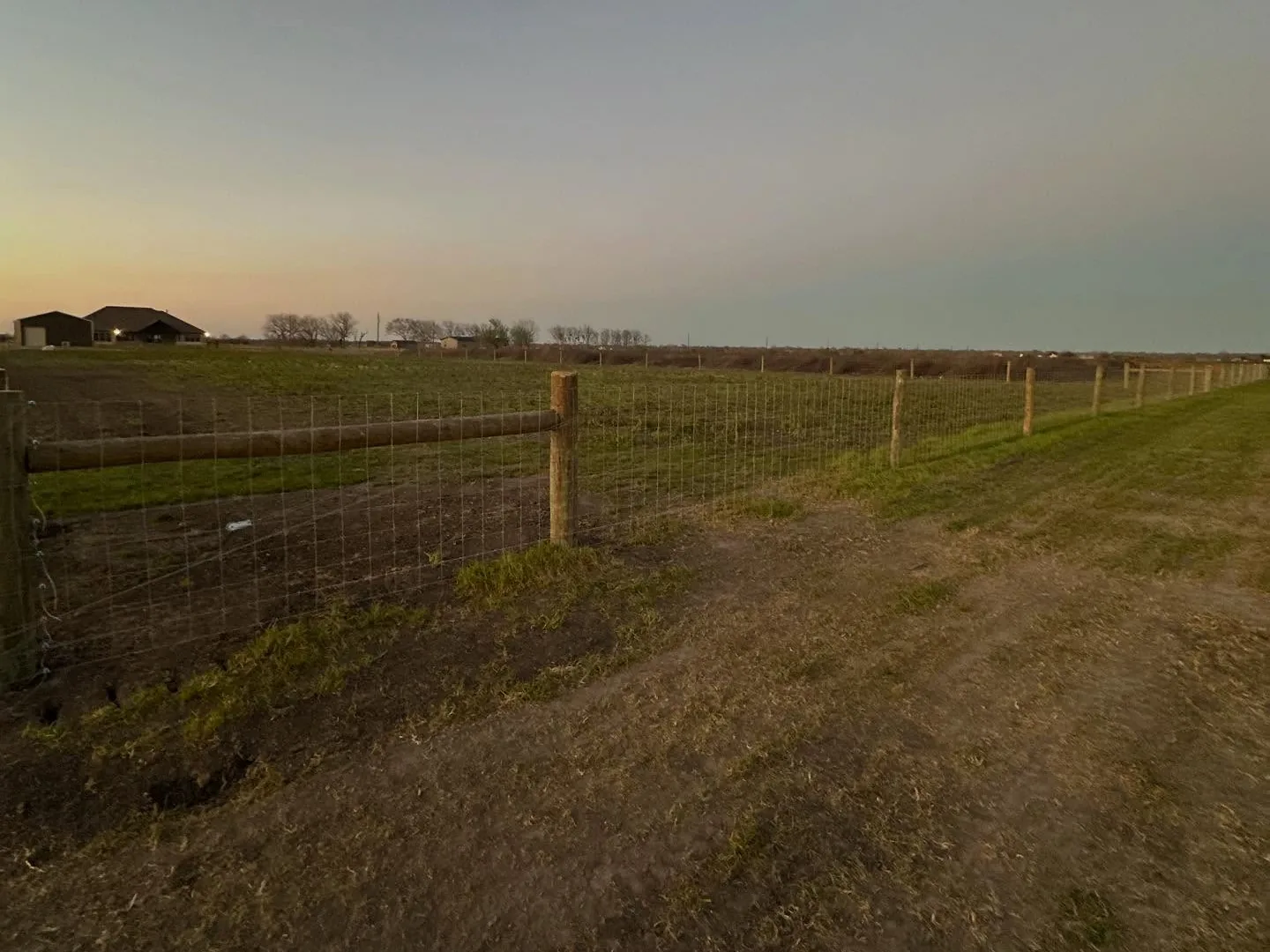 Clean wire fence line running across an open pasture, fence line clearing