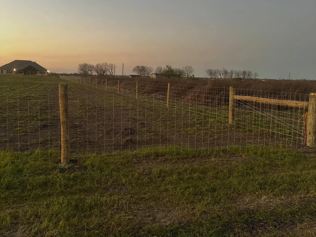 Woven wire fence on wood posts along a cleared pasture line, fence line clearing