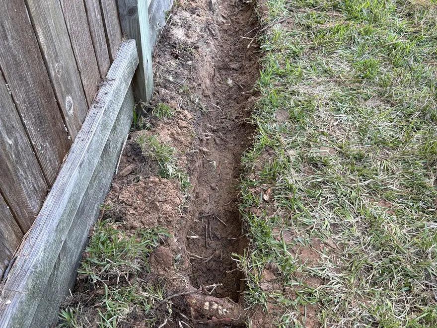 Trench dug along a wood fence for a French drain, French drain installation
