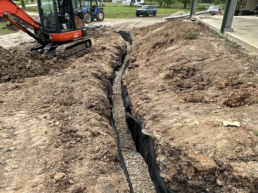 Mini excavator digging a drain line trench across a yard, French drain installation