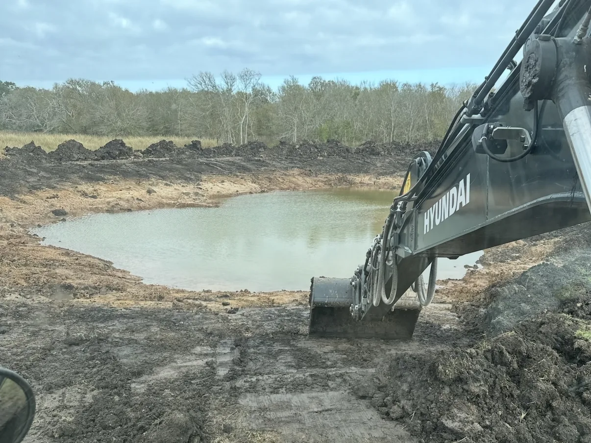 Excavator digging out a pond with water in the basin, pond construction