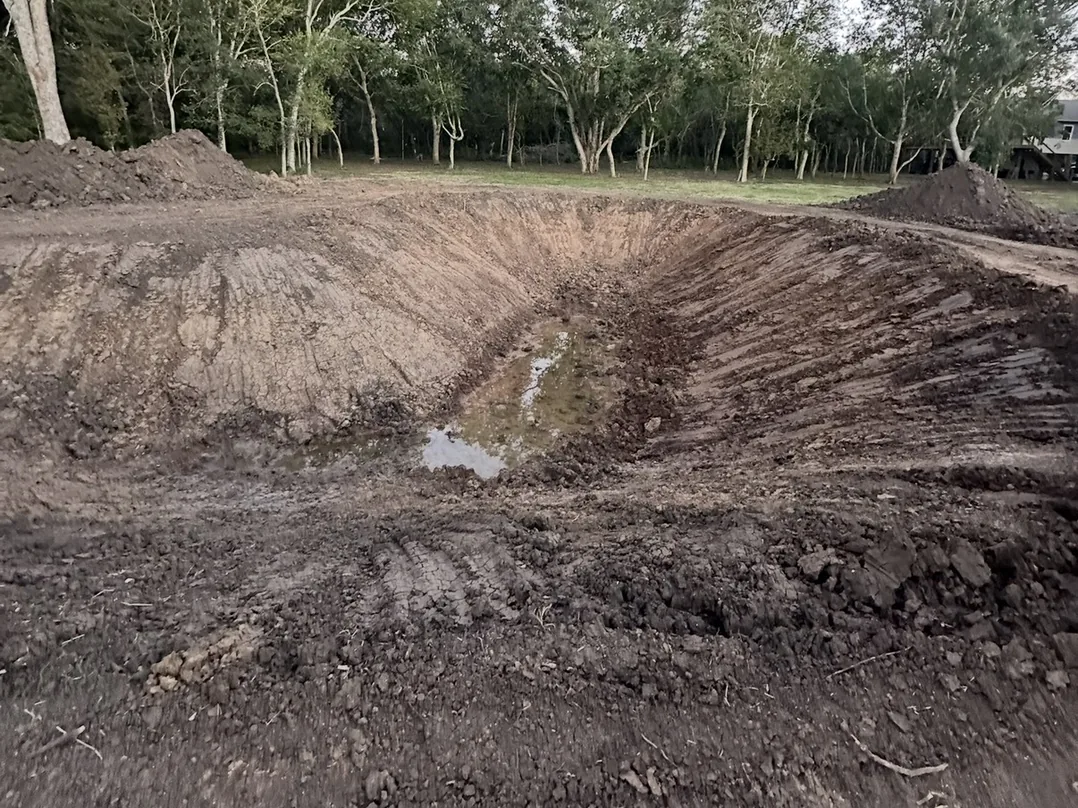 Freshly dug pond basin with sloped dirt banks, pond construction