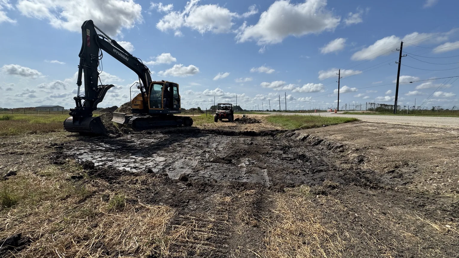 Excavator working a roadside ditch on open farm ground, culvert installation