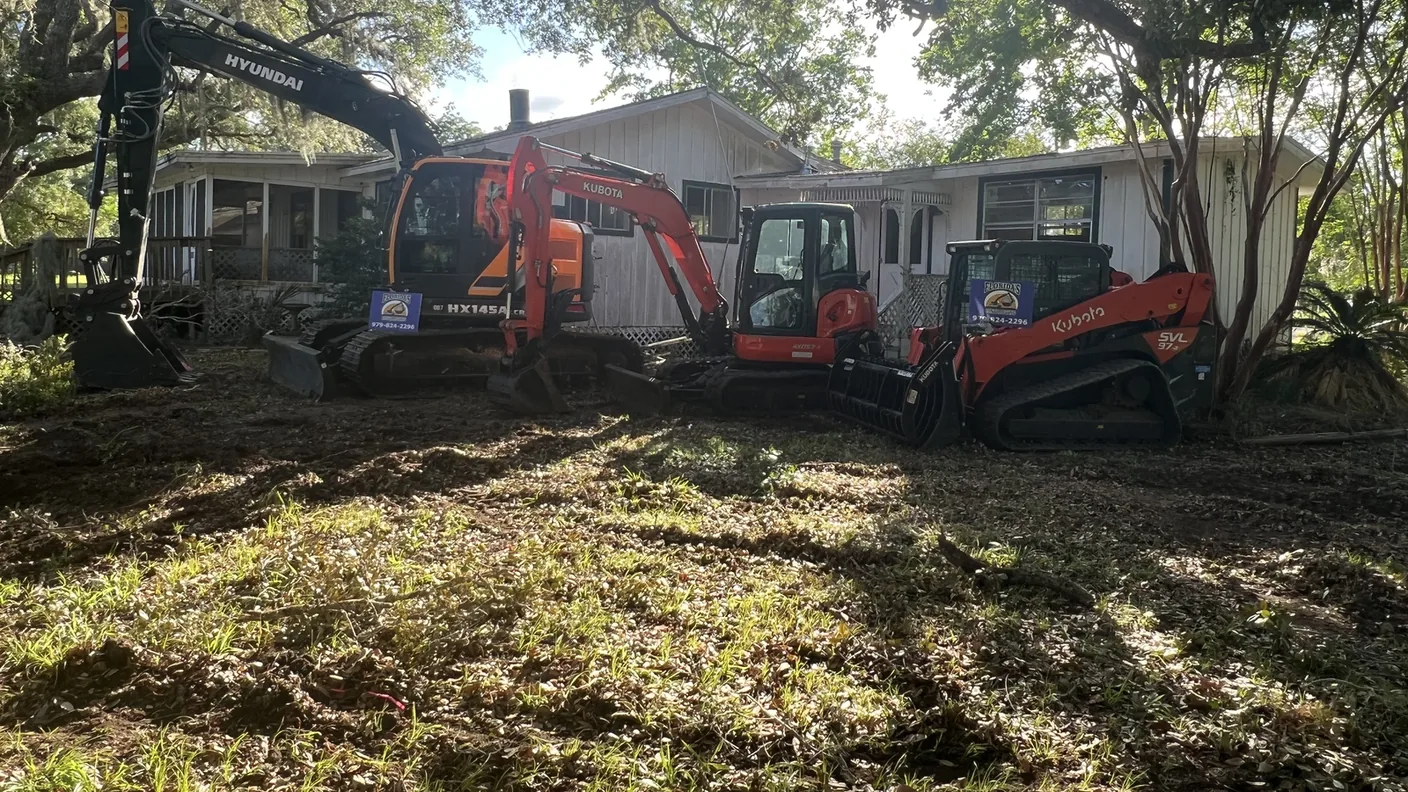Excavator, mini excavator and skid steer lined up on a cleared yard, land clearing